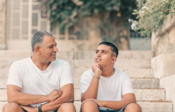 Senior father and his teenage son suffering from mental disability sitting on the stairs and chatting.