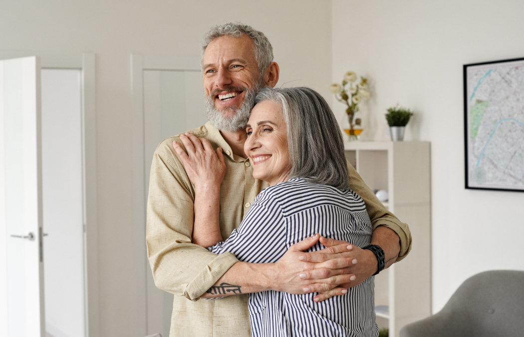 An older couple embraces and smiles in a modern living room with a map on the wall. Martinez, GA