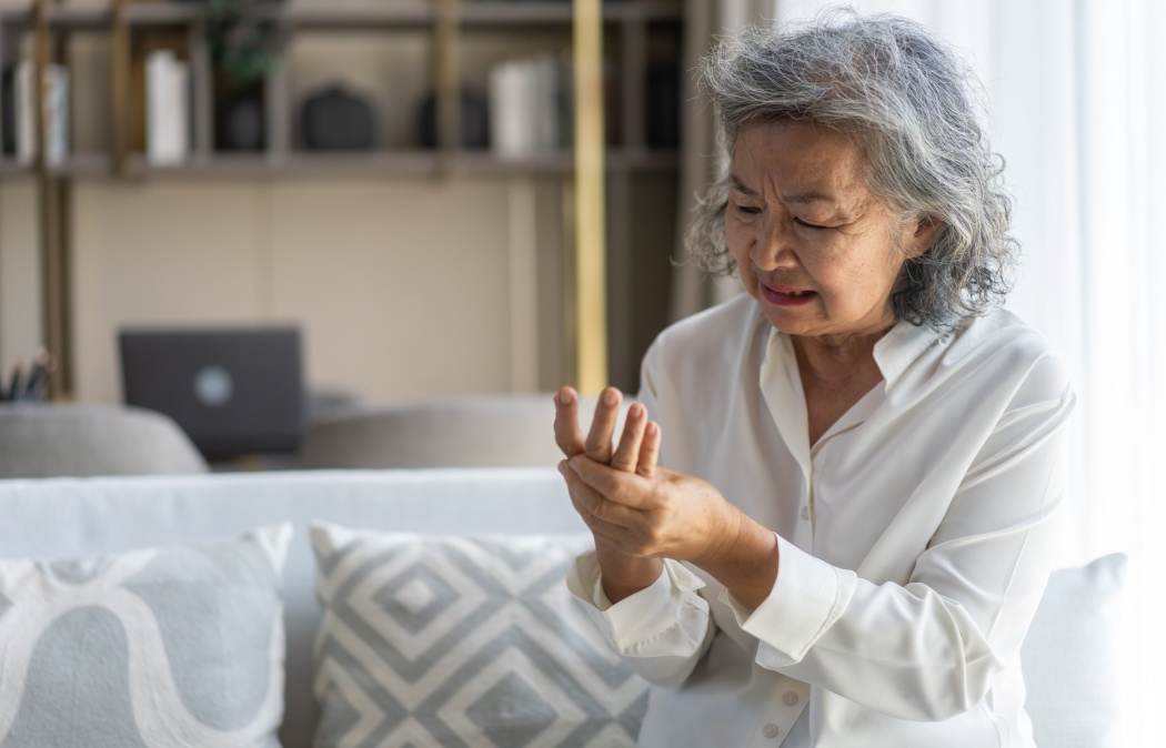 Elderly asian woman holding wrist pain, arthritis, health issue, senior female suffering from joint pain at home, expressing discomfort, aging health problem, chronic condition indoor living room Martinez, GA