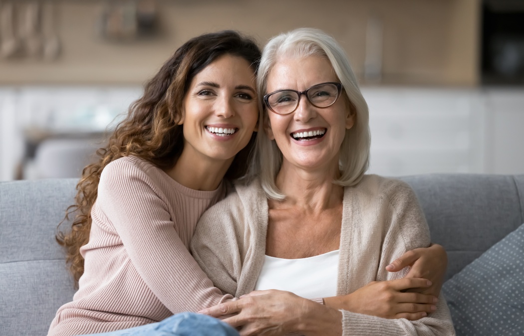 Portrait of two beautiful young and mature females, different generations women hugging sit on sofa, sharing warmth, joyful moments together. Family ties, intergenerational connection, love, support Martinez, GA